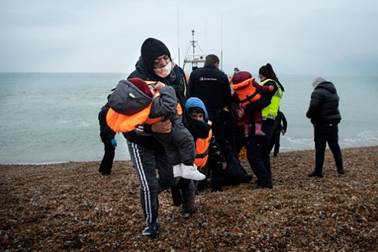 A migrant carries her children after being helped ashore from a RNLI (Royal National Lifeboat Institution) lifeboat at a beach in Dungeness, on the south-east coast of England, on November 24, 2021, after being rescued while crossing the English Channel. - The past three years have seen a significant rise in attempted Channel crossings by migrants, despite warnings of the dangers in the busy shipping lane between northern France and southern England, which is subject to strong currents and low temperatures. Photo: Getty Images / Ben STANSALL 